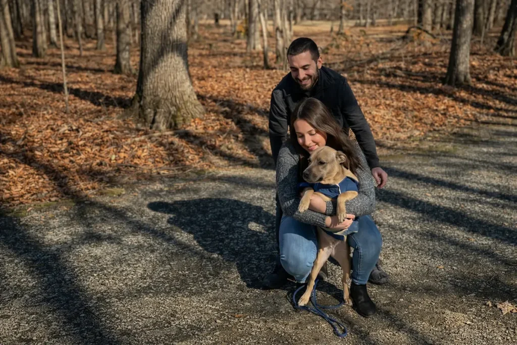 Smiling couple kneeling on a path holding their dog in a wooded park